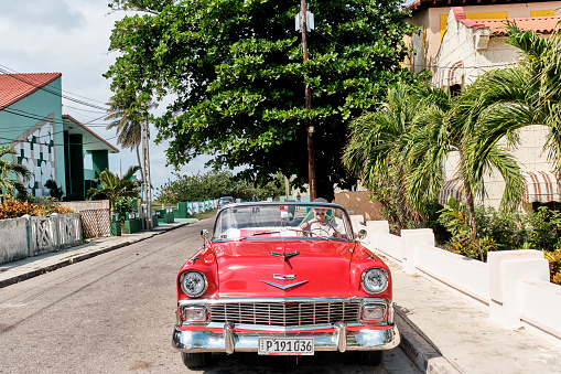 Varadero, Cuba - February 10, 2022: Man sitting in red and white retro 1957 Chevrolet car on street of resort town. Transport, travel concept