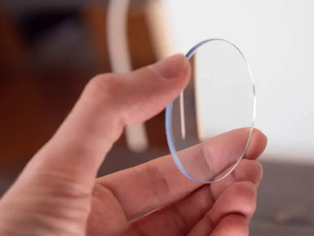 Photo of One clear lens, hand holds an eyewear round lens for quality control.