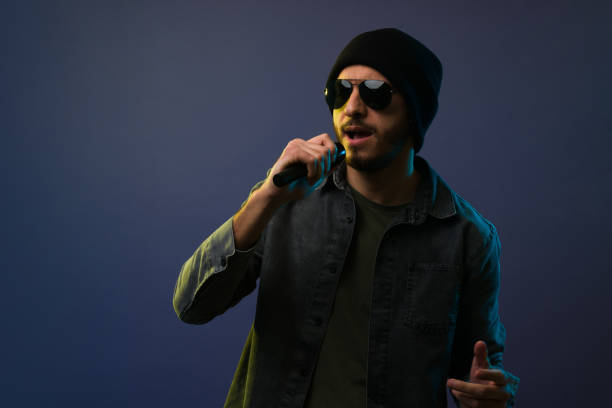 Attractive latin singer wearing a beanie hat and singing with a microphone a rap song against a studio background