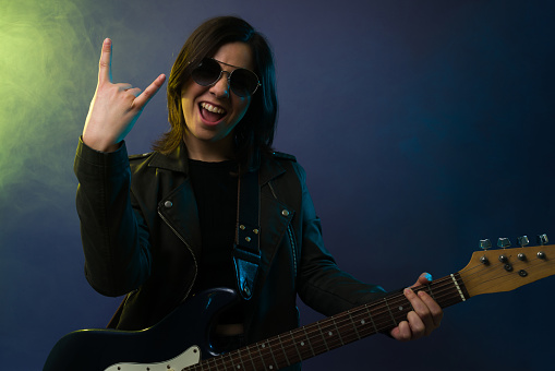 Rock and roll sign. Caucasian young woman playing the electric guitar against a background with smoke