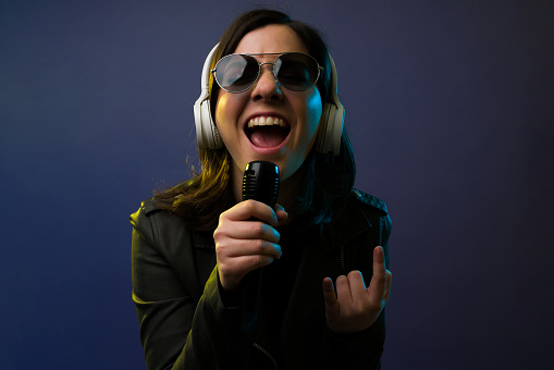 Hard rock music. Close up of an attractive female singer with headphones making the rock and roll sign while singing