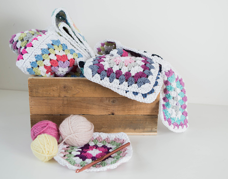 colorful granny sqaures with woolen balls and crochet hook in wooden box handmade