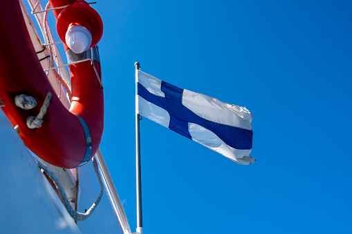 Finnish flag waving in the wind against blue sky. Orange lifebuoy is in the foreground.