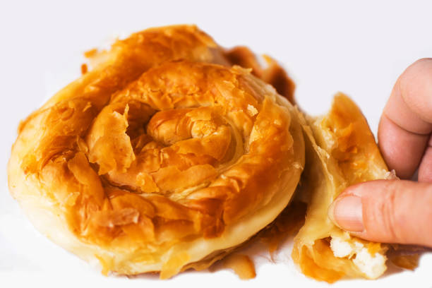 Spiral shape greek pie stuffed with cheese, made from filo dough. Hand holding broken piece. Called tyropita strifti, closeup.