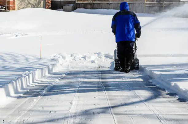 Man using a snow blower to clear a residential driveway after a snowfall