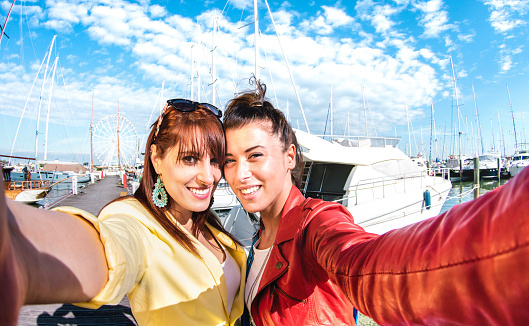 Happy women girlfriends taking fun selfie at sailboat docks - Friendship life style concept with best female friends catching the moment on smartphone point of view - Warm vivid filter