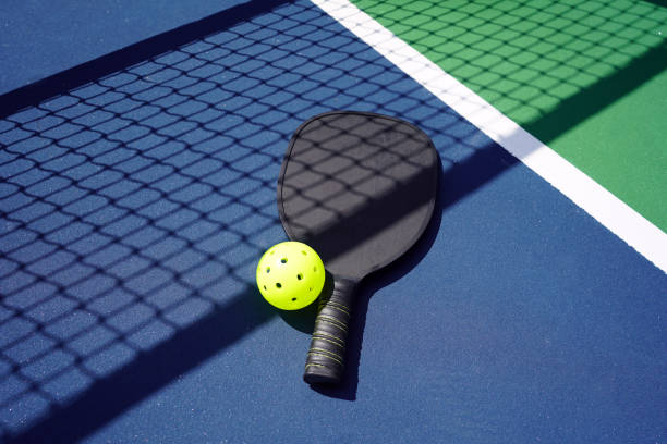 Pickle ball paddle on court Pickle ball paddle with ball on court with net shadow. pickleball stock pictures, royalty-free photos & images