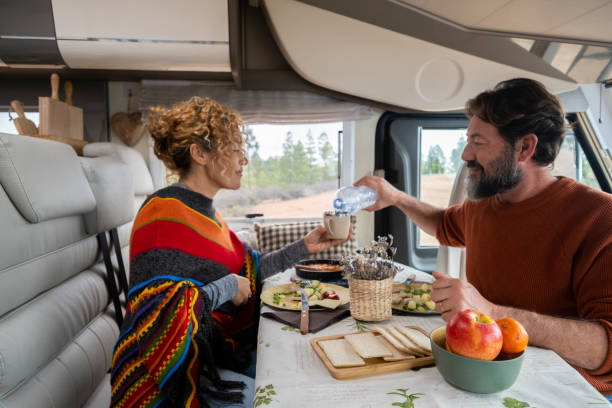 Adult couple enjoy time eating inside camper van in mountain holiday free vacation together. Man and woman in vanlife or tourist activity inside rv motorhome. Travel alternative home concept stock photo