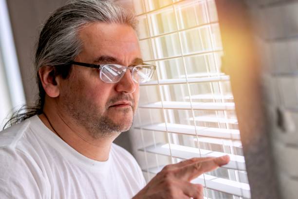 Serious, worried, stressed matura man looking through a window stock photo