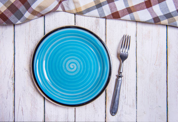 istock Top view background with empty blue ceramic plate, antique silver cutlery on vintage weathered white wooden boards. Copyspace. Brown checkered kitchen towel. 1373028870