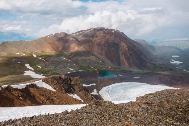 istock Dramatic landscape with contrast between sunny and rainy weather. Awesome scenery with sharp rocks and small lake in mountain valley. Changeable weather in mountains is sunny and cloudy at same time. 1373028966