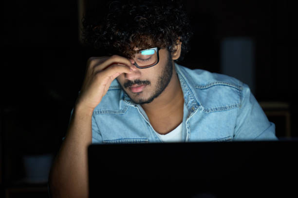 tired sleepy young indian man wearing glasses using computer working late. - 2779 imagens e fotografias de stock