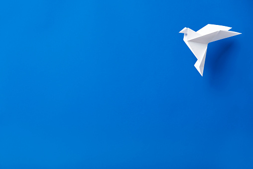 White origami paper dove flying against a blue background.