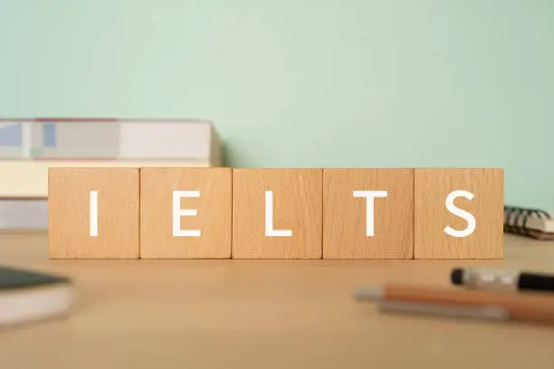 Wooden blocks with "IELTS" text of concept, pens, notebooks, and books.