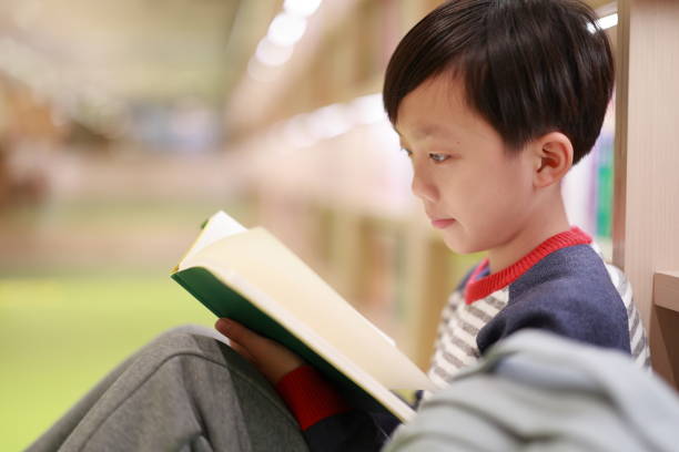 図書館のかわいい少年読書本 - bookstore student chinese ethnicity book ストックフォトと画像