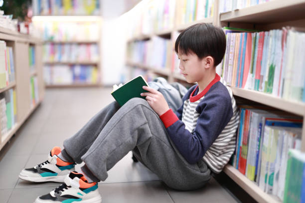 Cute boy reading book in library stock photo