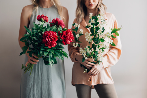 Two unrecognizable Caucasian women in elegant dresses, holding bouquets of flowers.