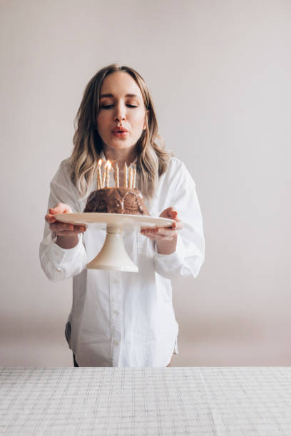 Happy Birthday! Beautiful Caucasian Woman in a White Shirt Blowing out Birthday Candles on a Gugelhupf Cake A happy Caucasian woman wearing a white shirt blowing out candles on her birthday bundt cake. woman birthday cake stock pictures, royalty-free photos & images