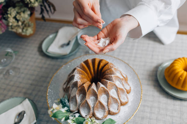 An anonymous Caucasian female pastry chef decorating a freshly baked bundt cake with powdered sugar.