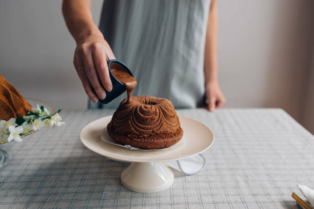 chef pastelera anónima vertiendo glaseado de chocolate sobre un pastel bundt - chocolate bundt cake fotografías e imágenes de stock