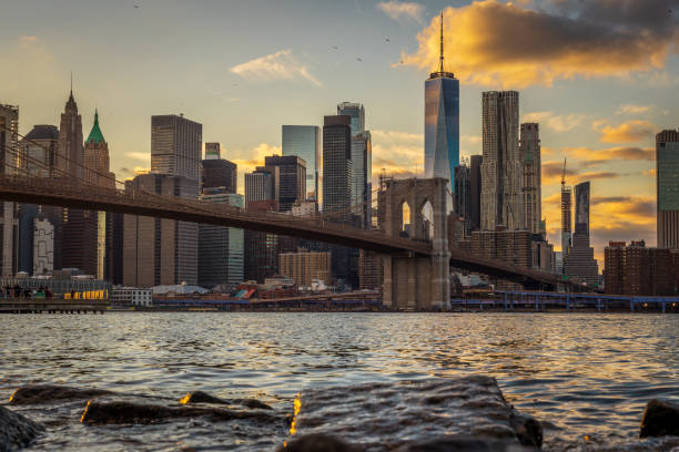 el puente de brooklyn y la torre de la libertad desde pebble beach en brooklyn bridge park - cityscape new york city manhattan low angle view fotografías e imágenes de stock