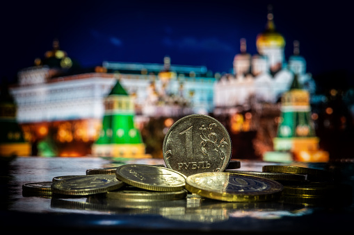 Moneda en denominación de 1 rublo ruso en una pila de otras monedas frente a fragmentos simbólicos fuera de foco del Kremlin de Moscú photo