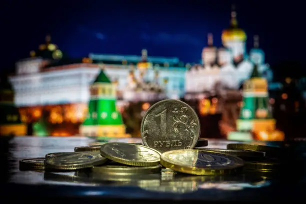Coin in denomination of 1 Russian ruble on a pile of other coins in front of symbolic out-of-focus fragments of the Moscow Kremlin