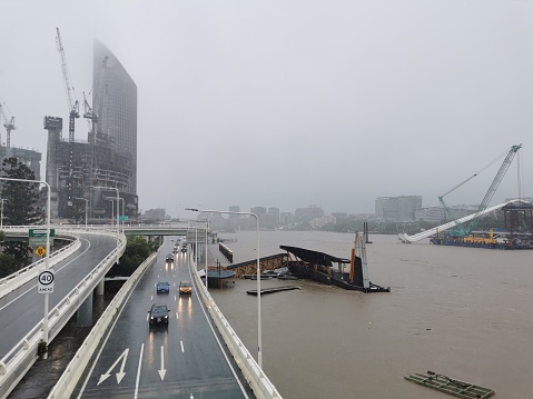 Brisbane, Australia - February 27, 2022: Wild weather and heavy rain falls from Tropical Cyclone storm Brisbane Central Business District. There are many cars drive on M3 highway. The North Quay ferry terminal is flooded and closed.