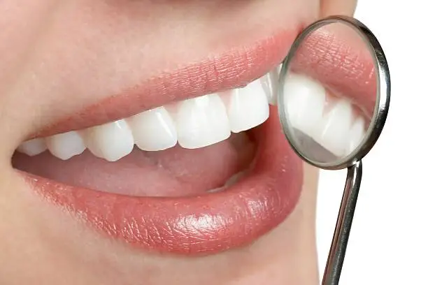 Photo of A woman smiling with a dental mirror close to her teeth