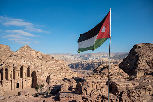 Black, white, green and red flag of Jordan flying over the tourist destination of Petra with The Monastery visible in the background