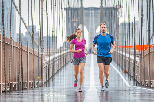 New York city runners athletes training for run marathon on Brooklyn Bridge. Fit active interracial couple on outdoor running exercise in raining day. Summer rain. Asian woman, Caucasian man.
