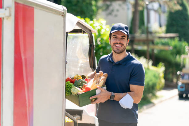 istock Delivering food ordered online while in home isolation during quarantine. Young courier wearing protective mask on his arm, delivering crate with fresh food to client. 1373064067