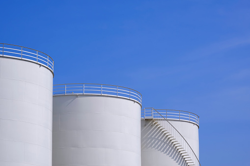 Three white oil storage fuel tanks against blue sky background, low angle view with copy space