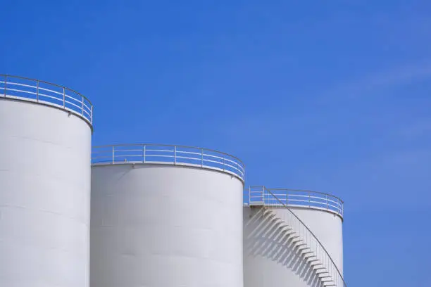 Photo of Three white oil storage fuel tanks against blue sky background, low angle view with copy space
