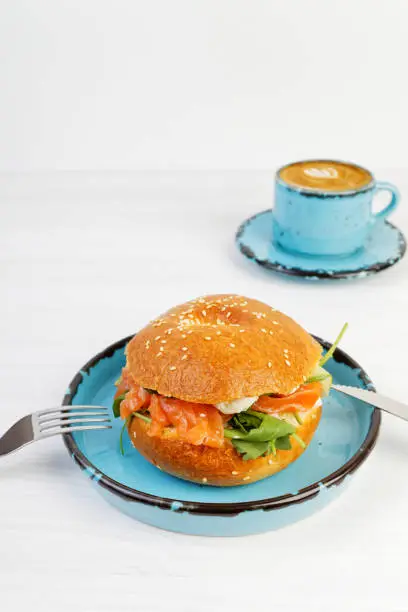 Bagel with salmon and cheese on white wooden table.