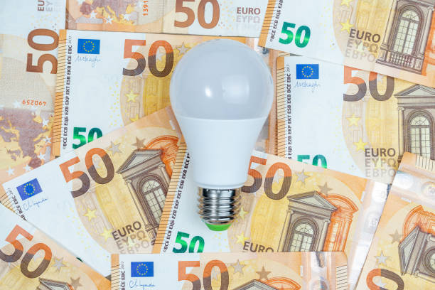 LED LIGHT BULB ON FIFTY EURO BANKNOTES ​BACKGROUND. ELECTRICAL ENERGY PRICES INCREASE. LED LIGHT BULB ON FIFTY EURO BANKNOTES ​BACKGROUND. ELECTRICAL ENERGY PRICES INCREASE. tarifa stock pictures, royalty-free photos & images