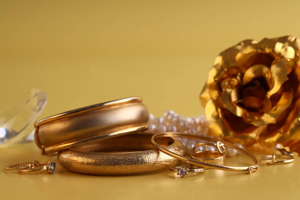 A large gold ring in the shape of a feather with sapphires lies next to a gold chain and other jewelry