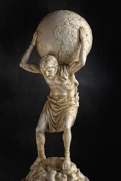A resin statue replica of the titan Atlas of Greek mythology carries the weight of the heavens on his shoulders.  Dramatic lighting help accentuate the detail in the torso and legs.
