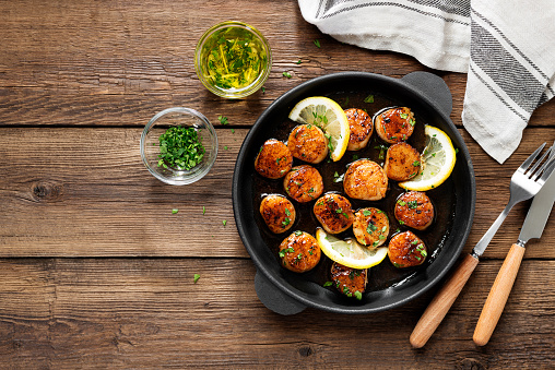 Grilled scallops with creamy lemon spicy sauce in a cast iron skillet on wooden background, top view