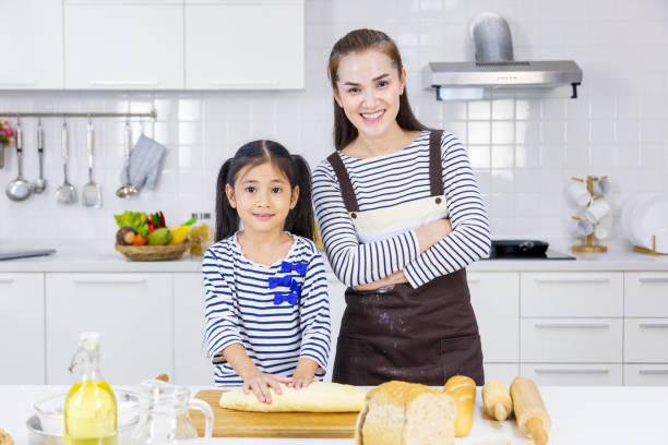 mãe asiática feliz ensinando sua filha jovem a assar pão na cozinha branca moderna enquanto amassa farinha para fazer massa - bread food baked 7 grain bread - fotografias e filmes do acervo