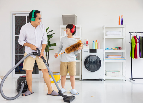 Asian father and son help each other to clean the house using vacuum machine for daily routine chores and housekeeping