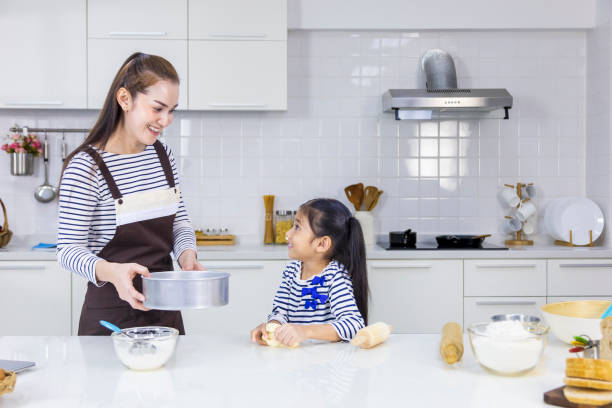 feliz madre asiática enseñando a su hija pequeña a hornear pan en la cocina blanca moderna mientras tamiza la harina de trigo para mezclar - bun bread 7 grain bread dough fotografías e imágenes de stock