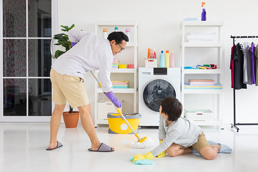 Asian father and son help each other to clean the floor using mop and bucket for daily routine chores and housekeeping