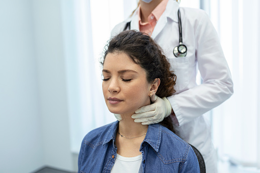 Endocrinologist examining throat of young woman in clinic. Women with thyroid gland test . Endocrinology, hormones and treatment. Inflammation of the sore throat