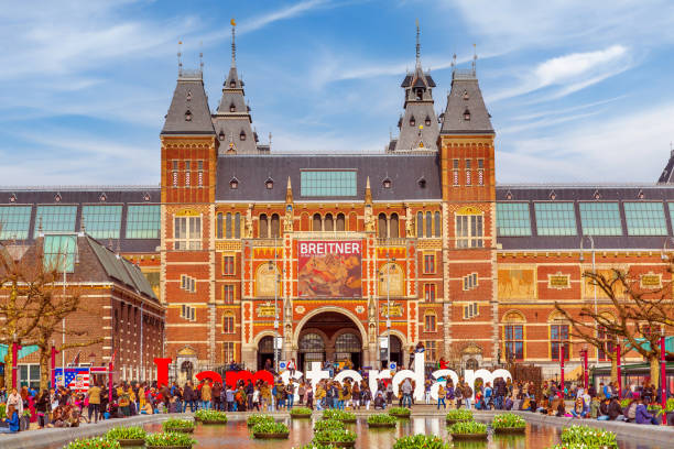 Rijksmuseum (The museum of the Netherlands) building facade with tourists and cyclists in the foreground on a bright summer autumn day in Amsterdam, Netherlands.The museum of the Netherlands, in Amsterdam has over 800 years of Dutch history, with the great dutch masters as Rembrandt, Vermeer and Van Gogh.