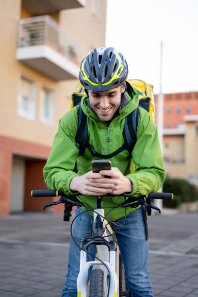 istock Smiling young man using bicylce to deliver boxes, documents and food at home, male courier using technology of smart devices to find address and sending work report 1373092236