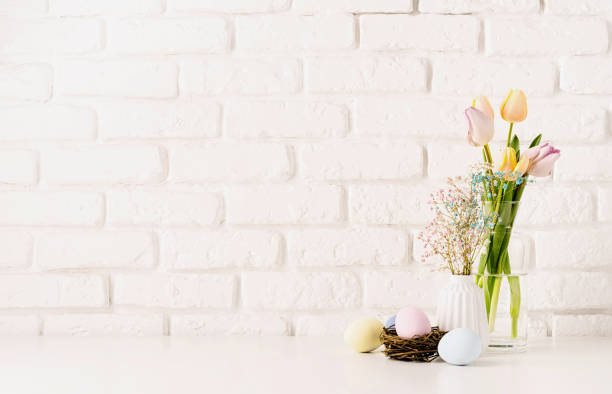 istock Fresh spring tulips in vase, gypsophila and pastel colored eggs on white brick wall background, copy space 1373093025