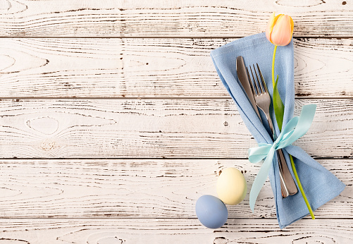 Happy Easter. Table setting for Easter feast. Easter eggs, tulips and cutlery top view flat lay on white rustic background