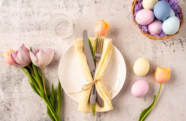 istock Table setting for Easter feast. Easter eggs, bunny, tulips and cutlery top view flat lay on concrete background 1373093843