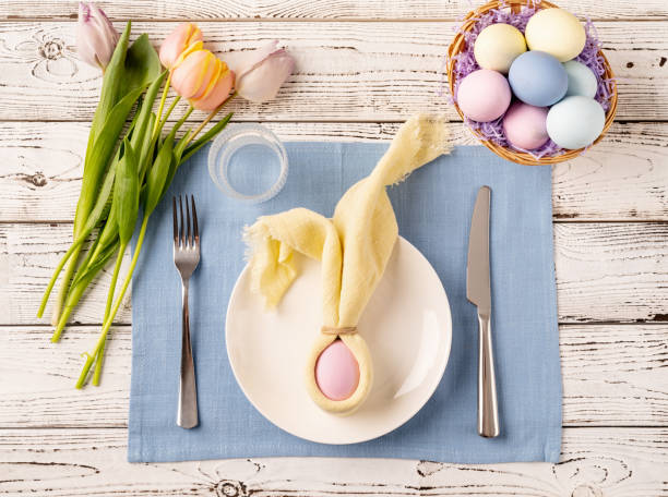 istock Table setting for Easter feast. Easter eggs, bunny, tulips and cutlery top view flat lay on white rustic background 1373093904